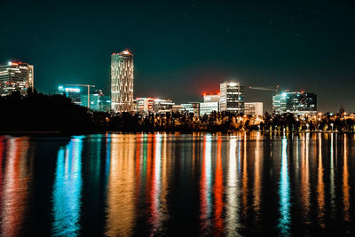 Illuminated buildings by river against sky at night