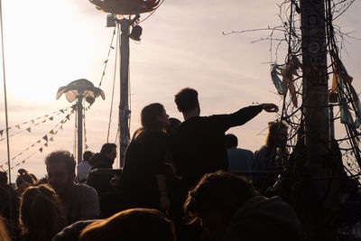 Silhouette people at amusement park against sky