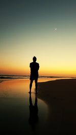 Silhouette man standing at beach against sky during sunset