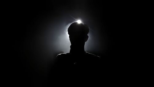 Rear view of silhouette woman standing against black background