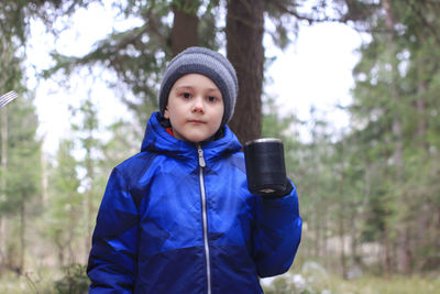 Portrait of boy against trees in forest during winter