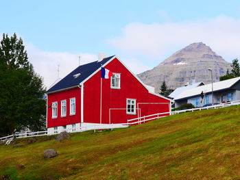 Red house on field by mountain against sky