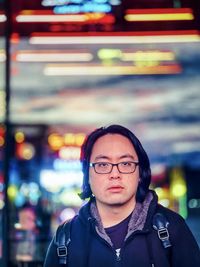 Portrait of young asian man standing against store window with reflection of neon lights in city.