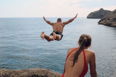 Woman looking at man diving into sea against sky