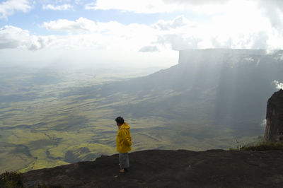 Rear view of man standing on mountain against sky