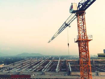 Crane at construction site against sky during sunset