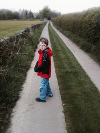 Full length portrait of boy standing on road against sky