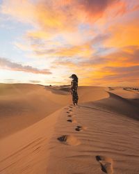 Woman standing on sand dune in desert against sky during sunset