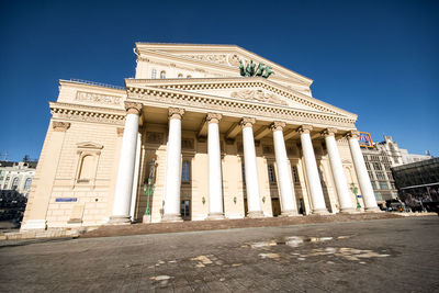 Low angle view of bolshoi theatre by street against blue sky