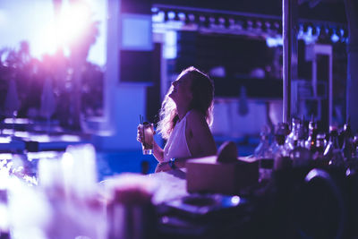 Young woman having drink at bar counter during sunset