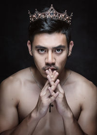 Close-up portrait of young man wearing crown against black background