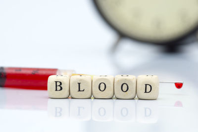 Close-up of toy blocks with text by syringe with blood against white background