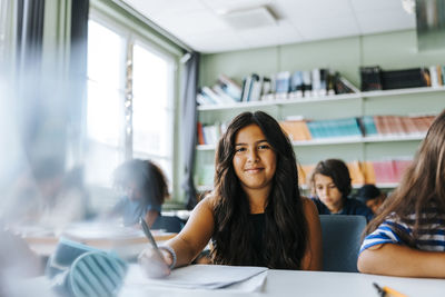 Portrait of smiling girl with long hair sitting in classroom at elementary school