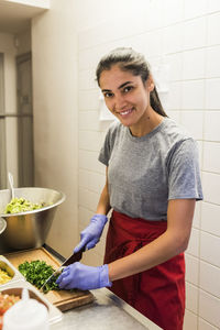 Smiling young chef chopping vegetable on cutting board in commercial kitchen at restaurant