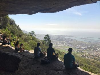 Rear view of people sitting on mountain against sky