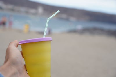 Close-up of hand holding drink at beach