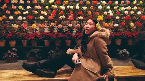 Portrait of young woman sitting by potted plants