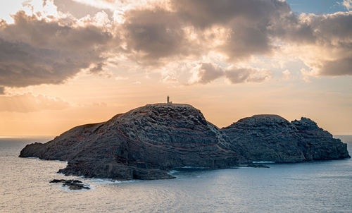 Rock formations by sea against sky during sunset