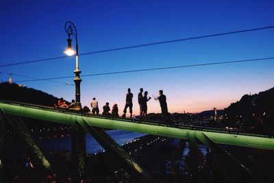 Silhouette people standing by illuminated water against clear sky
