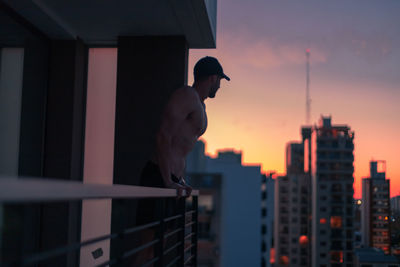 Shirtless man standing in balcony during dusk