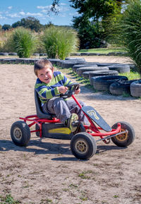 Laughing boy on a red pedal car plays on a dirt race track