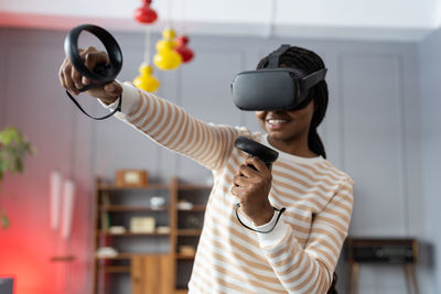 Happy young african american woman wearing virtual reality goggles playing video games at home