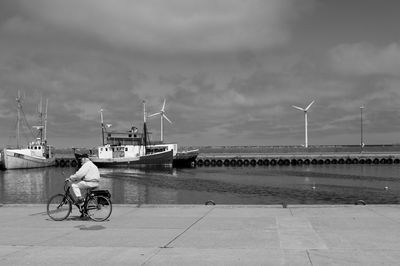 Man on bicycle by sea against sky