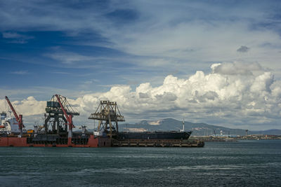 Cranes at commercial dock against sky