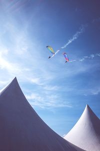 Low angle view of people paragliding against blue sky