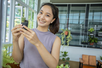 Portrait of smiling young woman showing potted plant