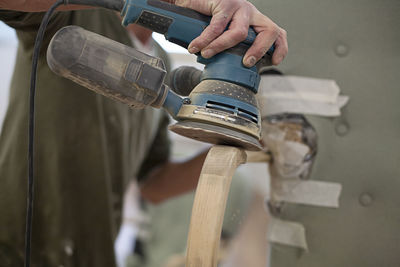 Close up view of someone power sanding the arm of an antique chair