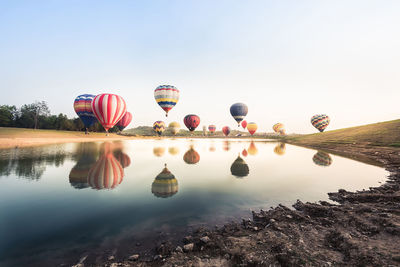 Reflection of hot air balloons in lake against clear sky