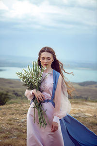 Woman stands on a mountain cliff in a blue long dress in summer