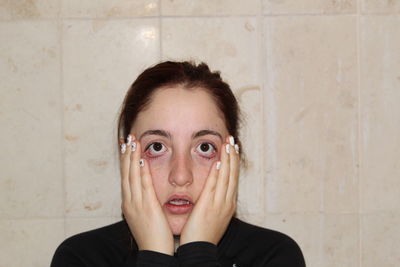 Portrait of shock young woman with hands on cheeks against wall