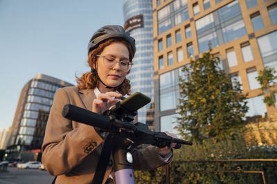 Businesswoman using mobile phone on electric push scooter in city