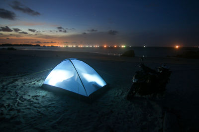 Illuminated light trails on beach against sky at night