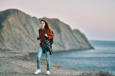 Young woman standing on rock at beach against sky