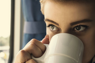 Close-up portrait of young woman drinking from window