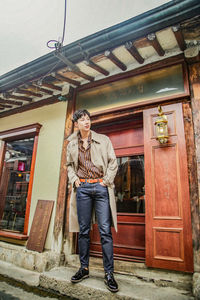 Full length portrait of young man standing against building