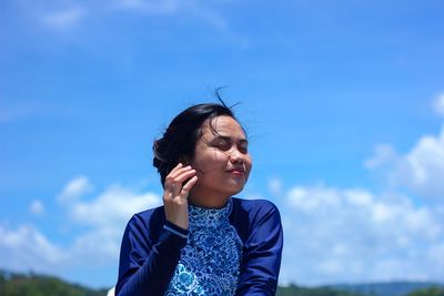 Woman with eyes closed standing against blue sky