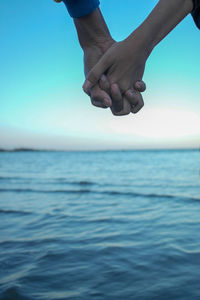 Person hand in sea against sky