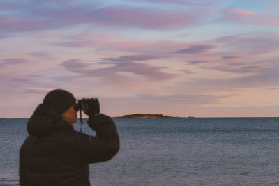 Side view of woman photographing sea against sky during sunset