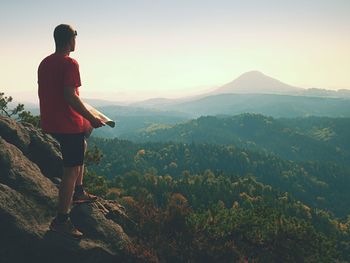 Man standing on rock looking at mountains against sky