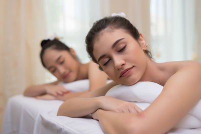 Young female friends lying with eyes closed on massage tables in spa