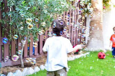 Rear view of boy playing with bubbles at backyard