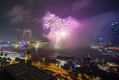 Firework display over river in illuminated city at night