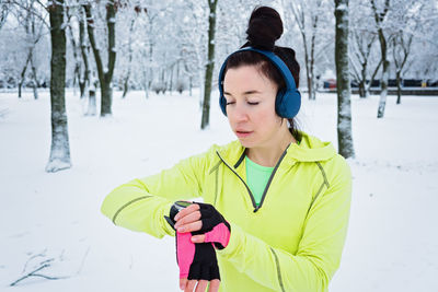 Running woman looking at smartwatch, checking heartrate and pulse during jogging in winter park