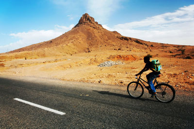 Side view of man cycling on road by mountain