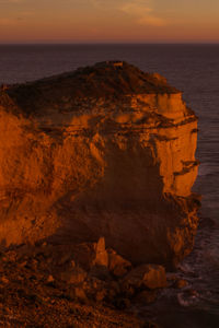 Rock formation in sea against sky during sunset