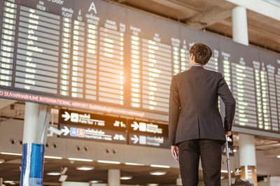 Rear view of businessman looking at departure board in airport